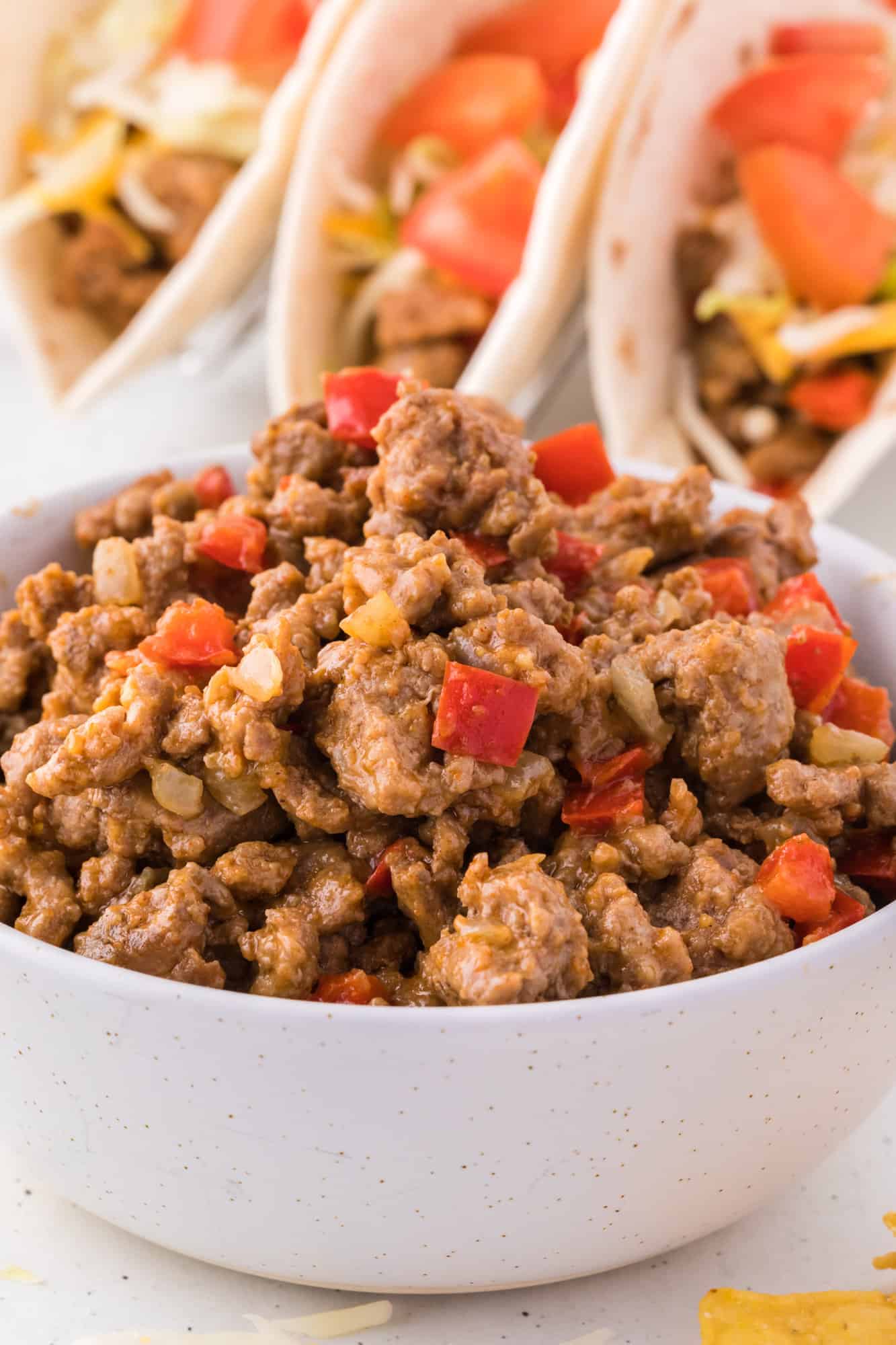 Ground turkey taco mean in a white bowl, with tacos in the background.