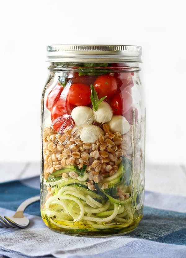 Layered salad in Mason jar with lid on, fork and blue plaid cloth is pictured.