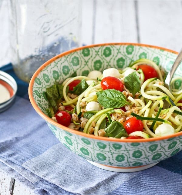 Green patterned bowl with mixed salad in foreground, empty jar in background on blue plaid cloth.