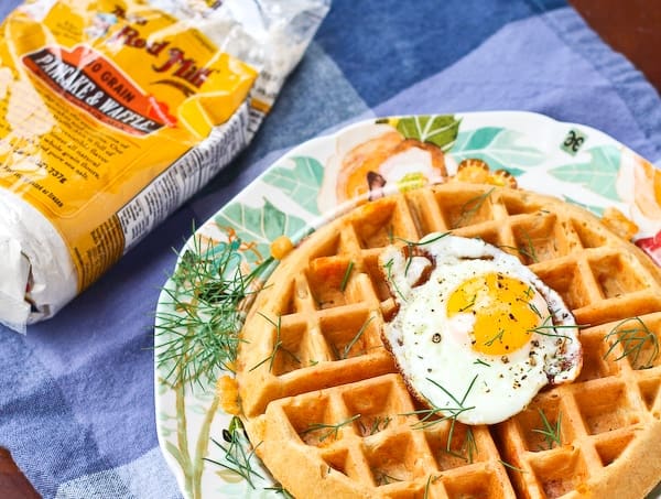 Image of waffle on decorative plate topped with fried egg.
