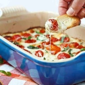 Piece of bread dipping into melted cheese and warm tomatoes.