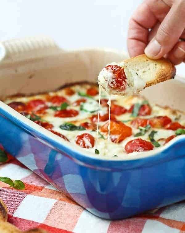 Piece of bread dipping into melted cheese and warm tomatoes.