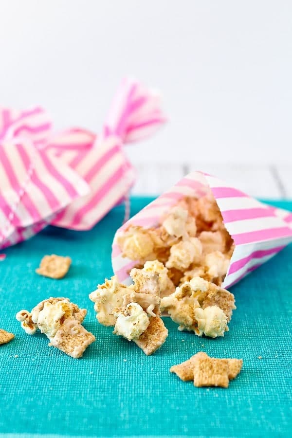 Cinnamon popcorn spilling out of pink striped treat bag onto turquoise cloth surface.