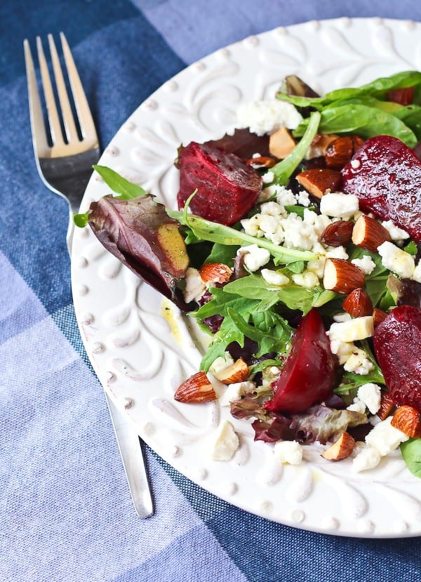Partial overhead of salad arranged on decorative white plate, with fork alongside on blue plaid cloth.