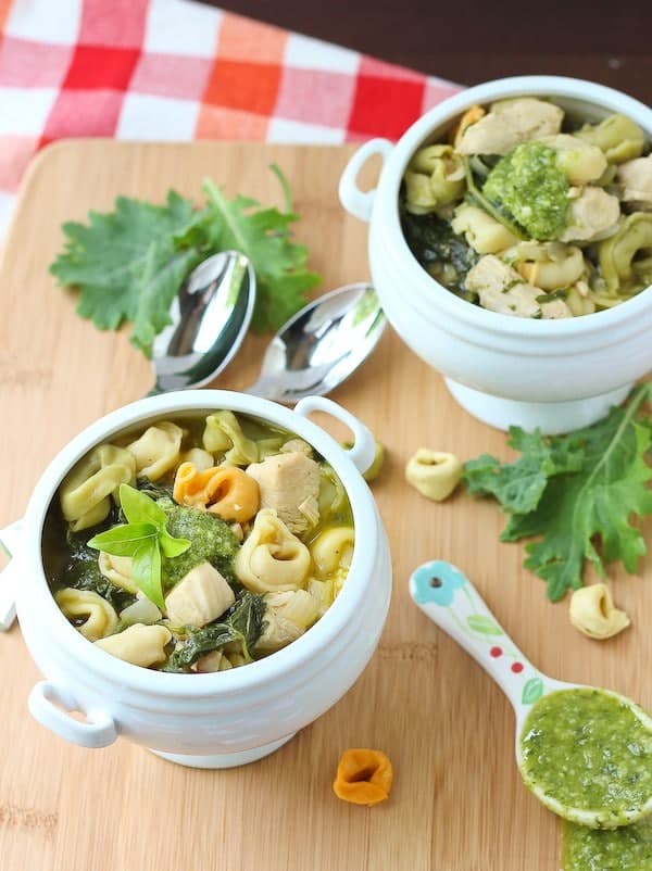 Overhead of chicken tortellini soup in two serving bowls garnished with pesto and basil leaves.