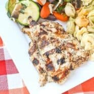 Partial overhead of plated grilled chicken dinner with vegetables and pasta.