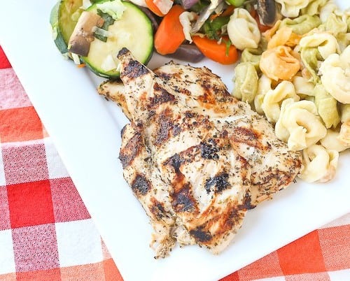 Partial overhead of plated grilled chicken dinner with vegetables and pasta.