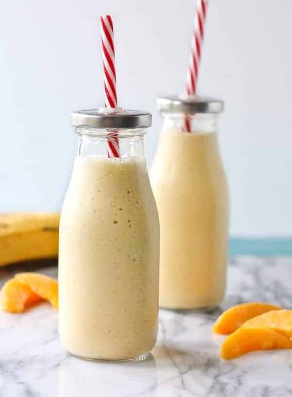 Two cottage cheese and peach smoothies with straws.