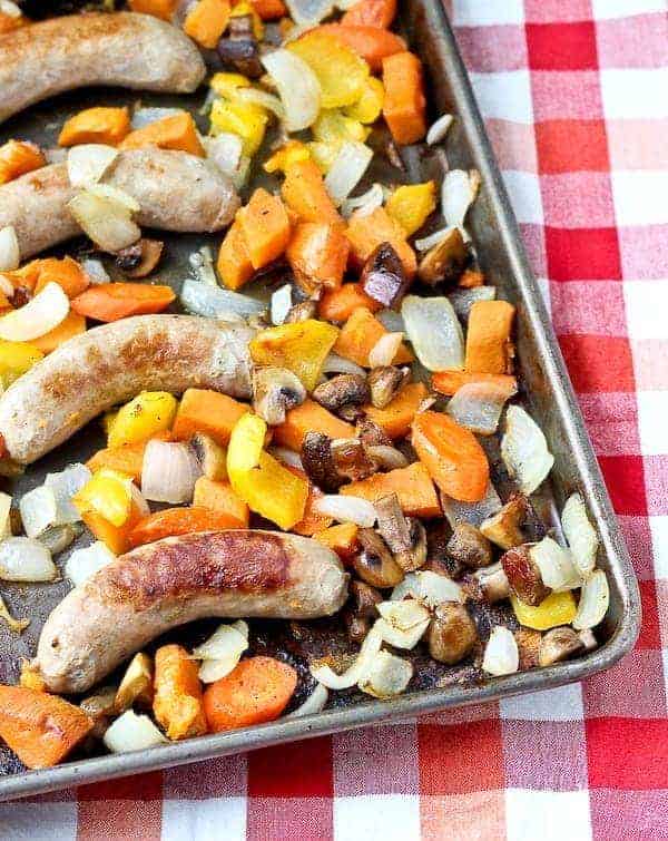 Sheet pan with roasted sausage and vegetables on red checked cloth.