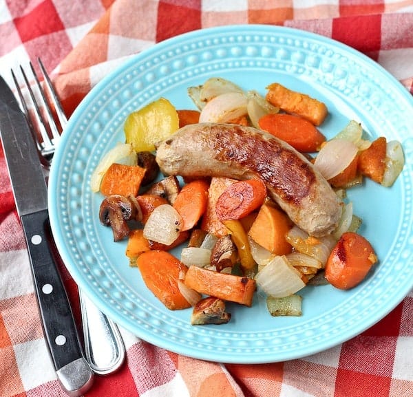 Roasted sausage and vegetables on decorative plate with fork and knife.