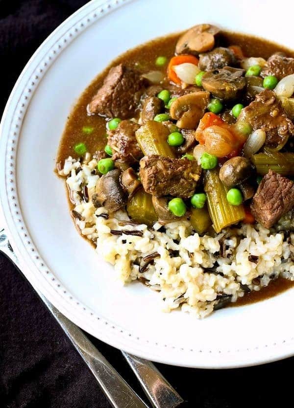 Overhead of beef stew in shallow white bowl, with white rice.