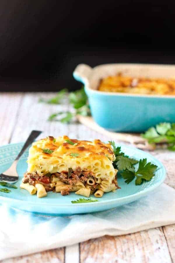 A serving of pastitsio on a decorative plate, garnished with parsley leaves, with fork alongside.