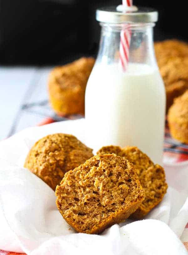 Two halves of a pumpkin bran muffin on a white cloth, with a glass of milk in the background.