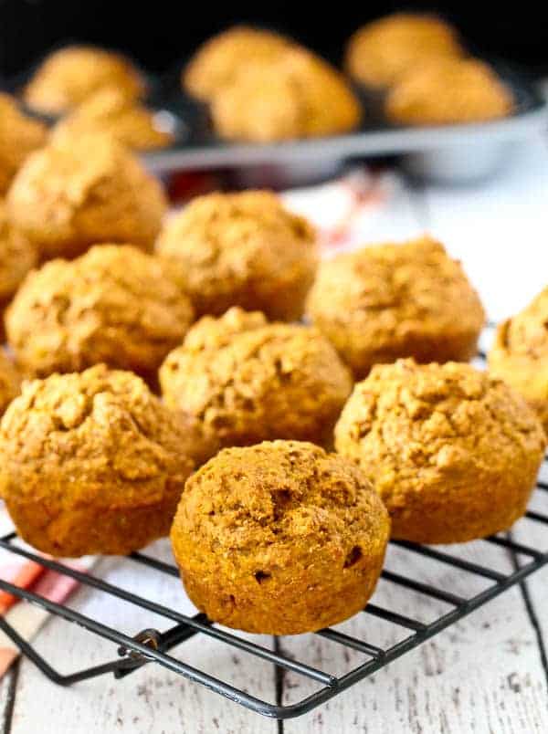 Pumpkin bran muffins on a wire rack, with more muffins in a muffin pan in the background.