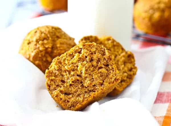 Two halves of a pumpkin bran muffin on a white cloth, with a glass of milk in the background.