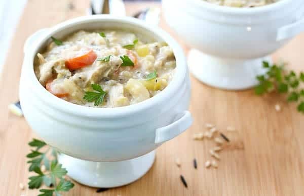 Footed white soup bowl containing chicken rice soup, garnished with fresh parsley sprigs.