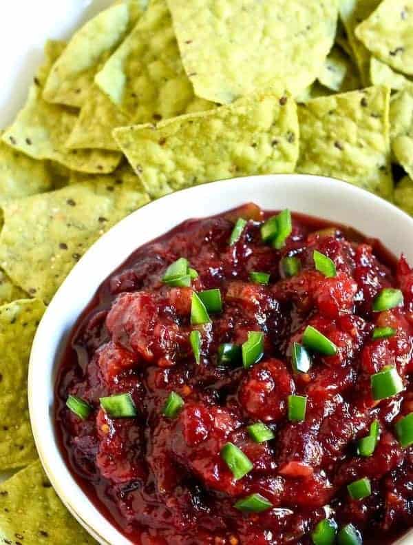 Bright red salsa in a bowl surrounded by green tortilla chips.