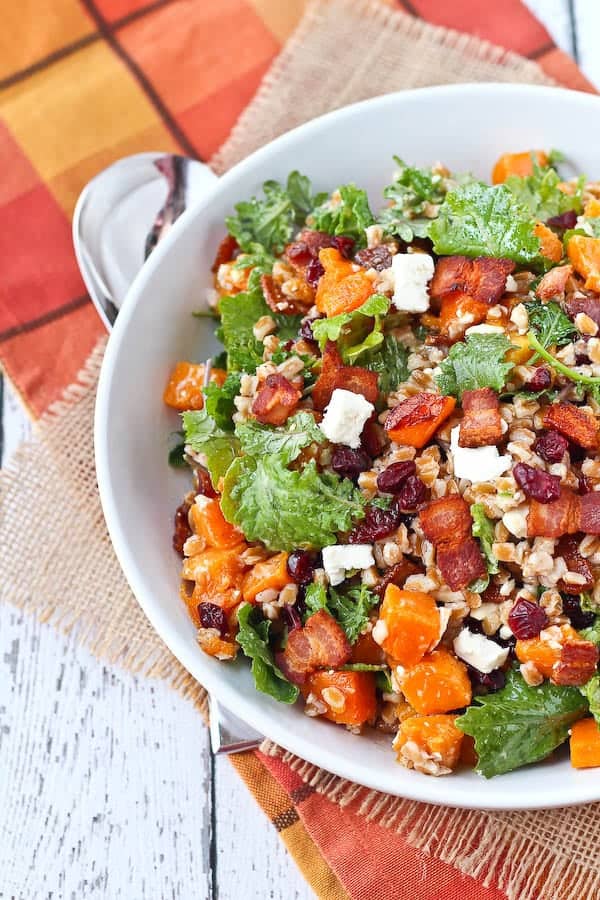 Overhead of round white bowl with farro salad, on burlap and plaid cloth in fall colors.