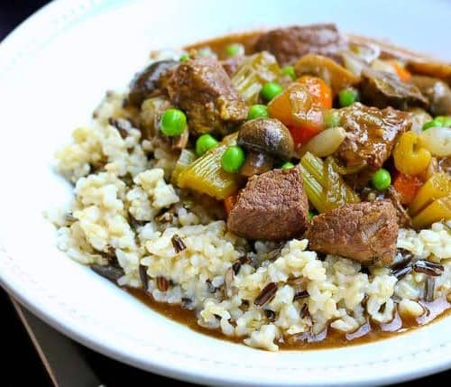 Beef stew in shallow white dish served with white rice.
