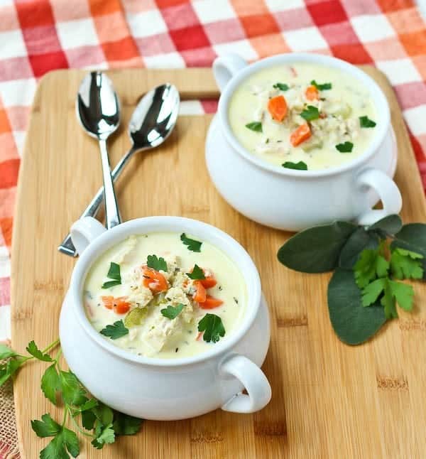 Two servings of turkey soup in white bowls with handles, garnished with fresh herbs.