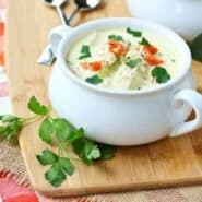 A serving of turkey soup in white bowl with chopped parsley.