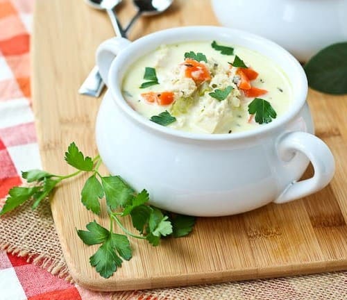 A serving of turkey soup in white bowl with chopped parsley.