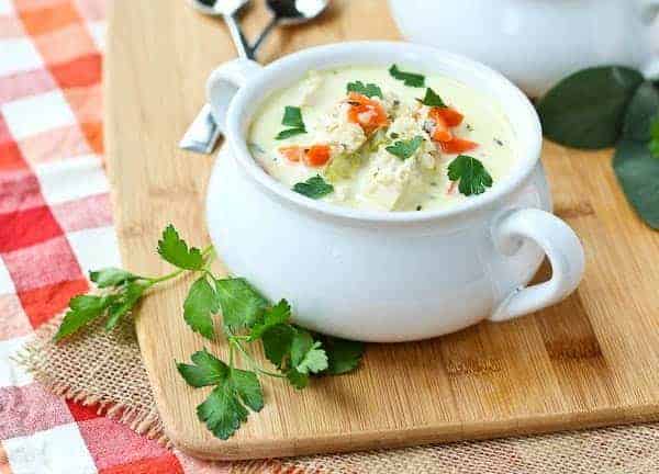 A serving of turkey soup in white bowl with chopped parsley.