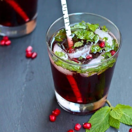 Front top view of pomegranate mojito in clear glass tumbler with white birch straw.