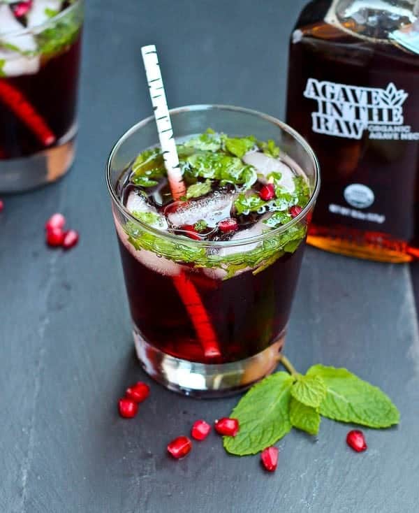 Front top view of pomegranate mojito, with bottle of Agave In The Raw in the background.