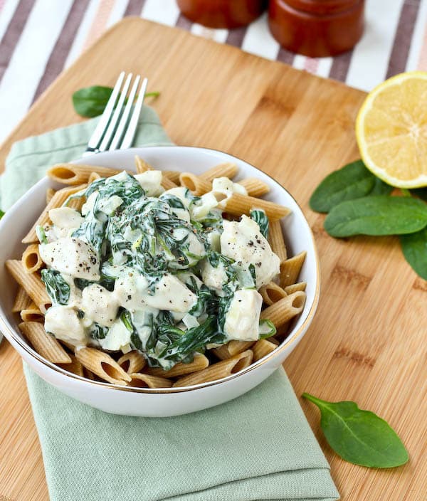 Serving of chicken and spinach pasta in round white bowl with fork and pale green napkin.