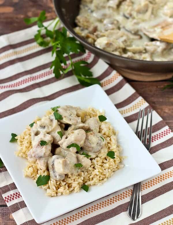 Overhead of serving of chicken on rice, garnished with parsley in square white plate.