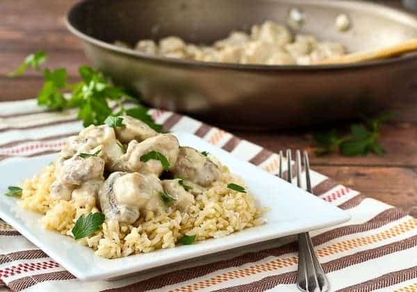 Serving of chicken on rice with skillet in background.