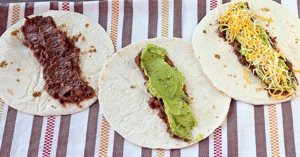 Three open face tortillas spread with black beans, guacamole, and sprinkled with cheese.