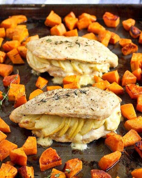 Two stuffed chicken breasts on sheet pan with roasted sweet potatoes.