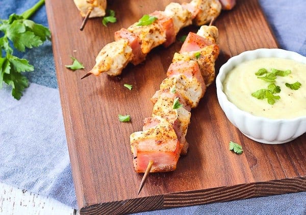 Partial overhead of kababs on wooden board with sauce.