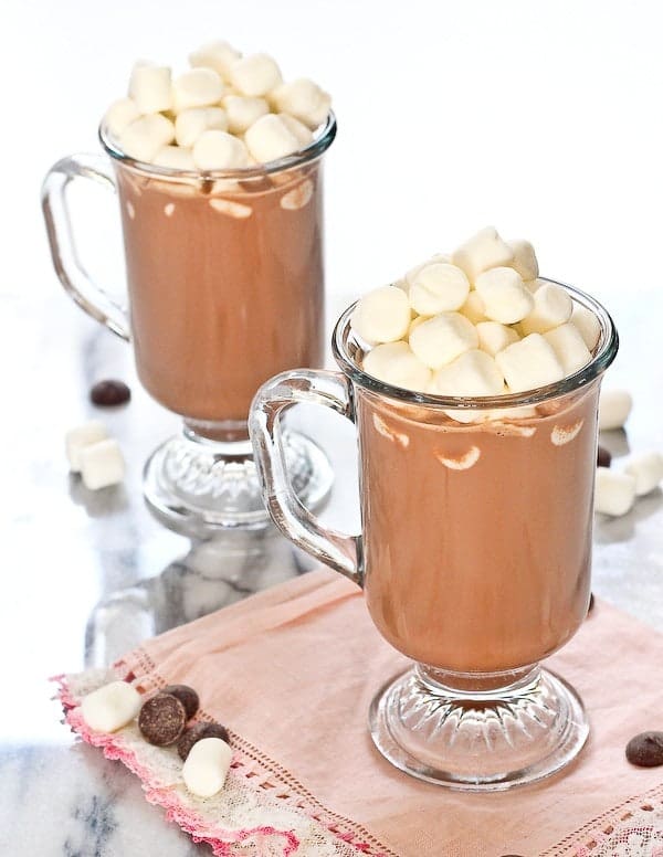 Two footed glass mugs of hot chocolate loaded with mounds of mini marshmallows. 