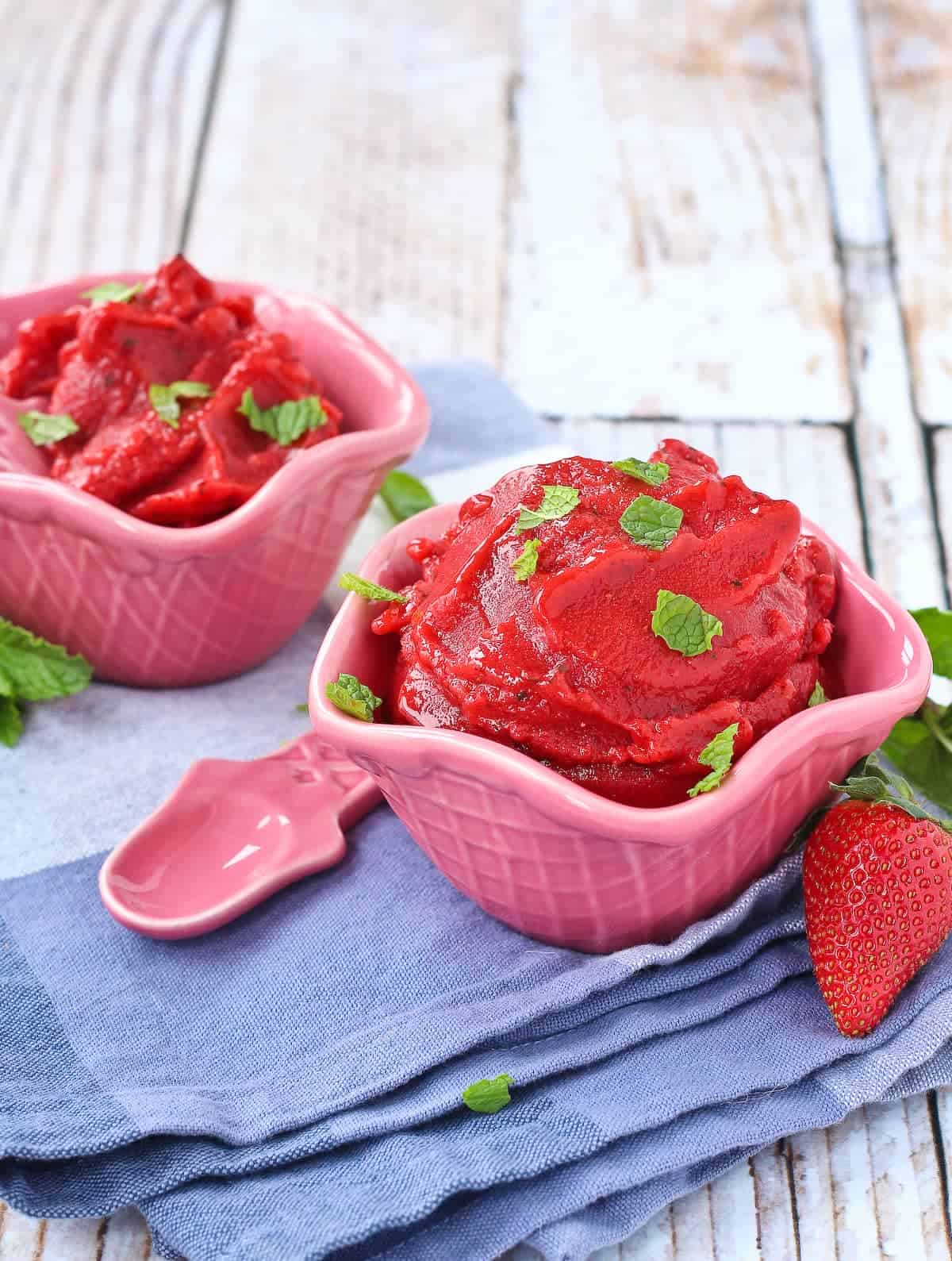 Strawberry sorbet in pink ice cream bowls, topped with fresh mint.