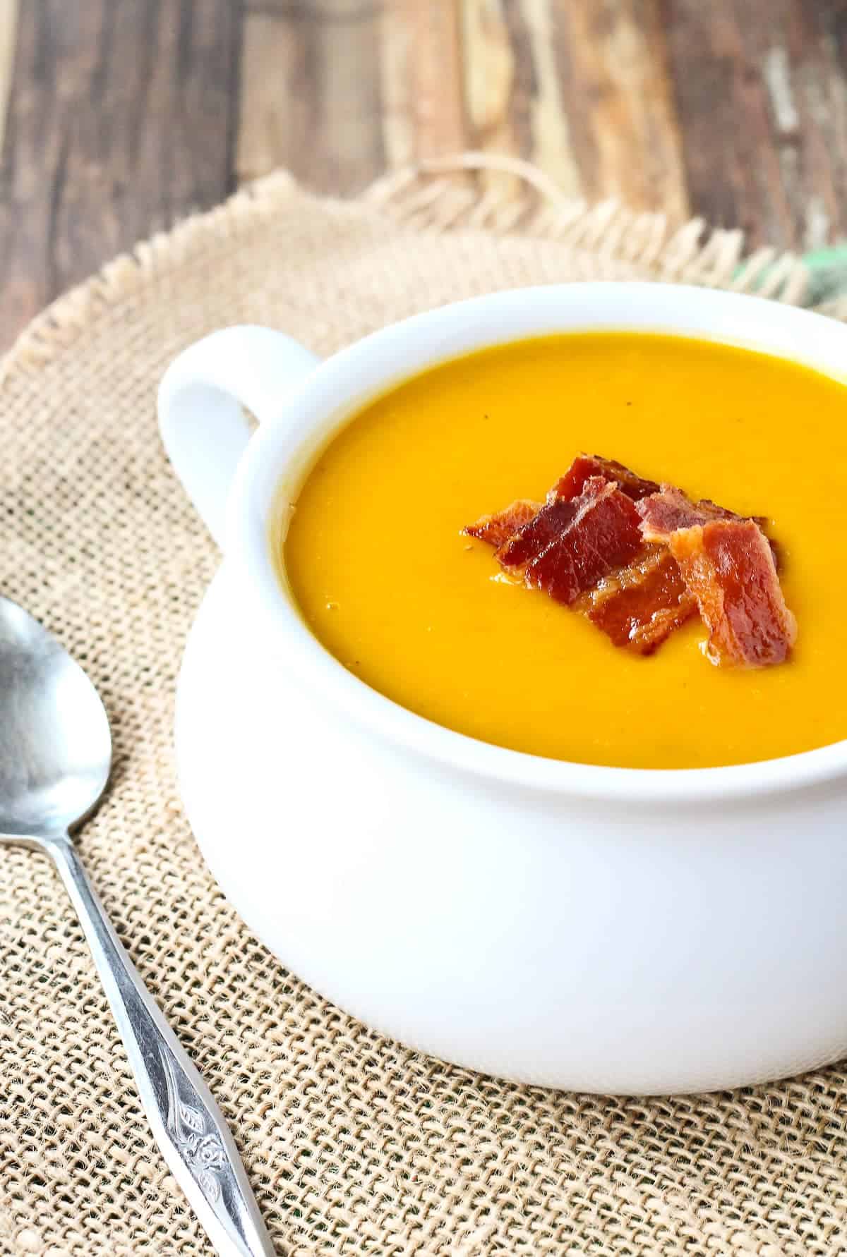 Butternut squash soup in a white bowl topped with crispy bacon pieces.