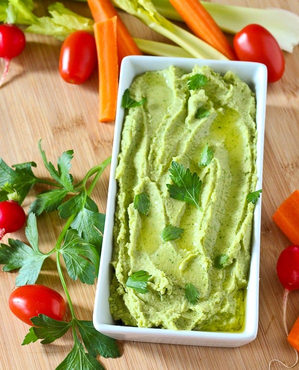 Overhead of hummus in serving dish on bamboo surface.