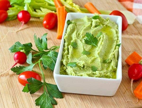 Hummus in serving container, with fresh veggies scattered around.