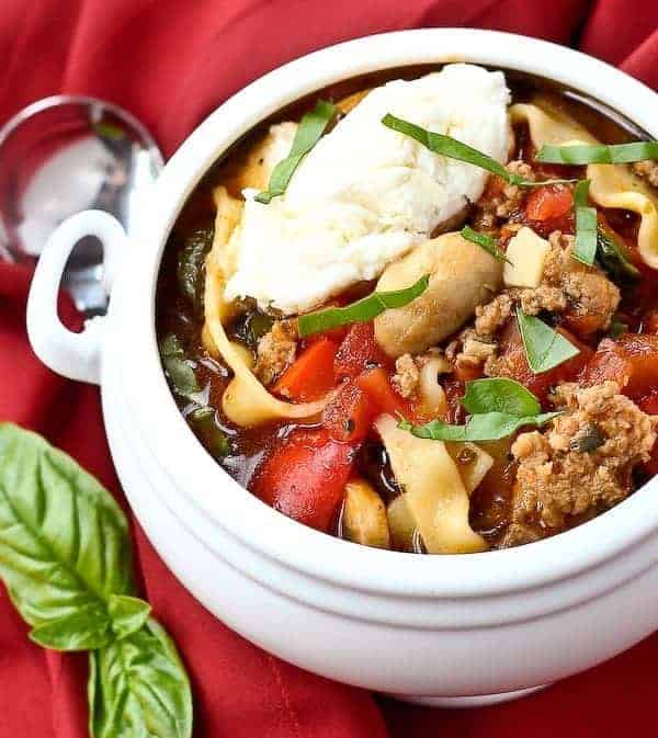 Serving of lasagna soup in white bowl with handles, garnished with basil strips.