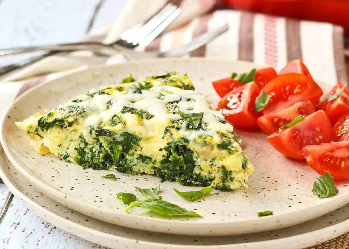 Slice of frittata on a plate, cut to show spinach and cheese.