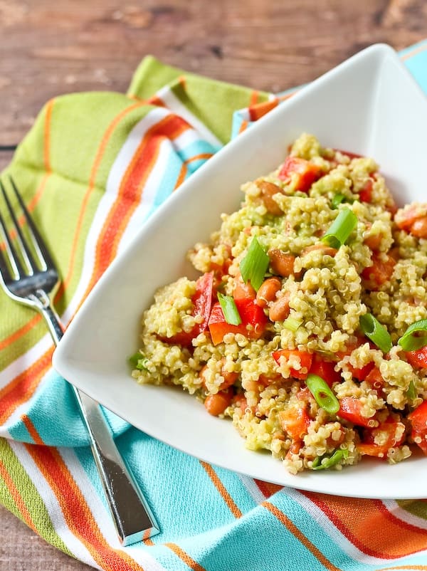 Quinoa salad with avocado dressing and red bell peppers in a triangle shaped bowl.
