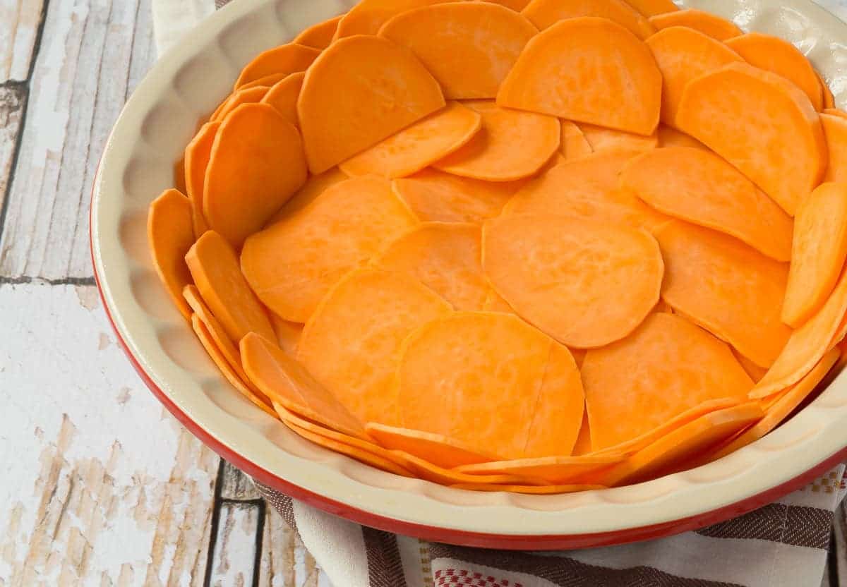 Closeup of sweet potatoes layered in pie dish to make crust, prebaked.