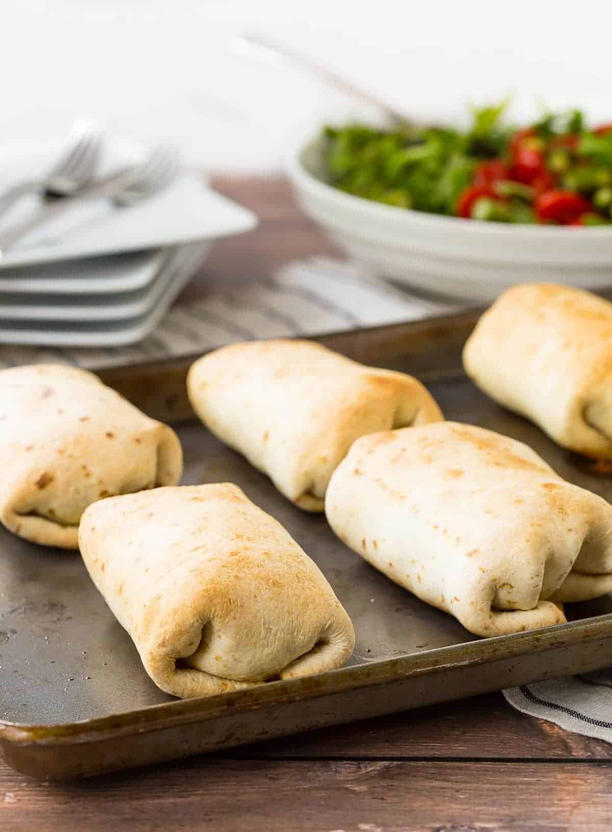 Several baked chimichangas on sheet pan.