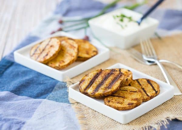 Grilled potato slices on small square white plates, along with forks and square dish of sour cream.