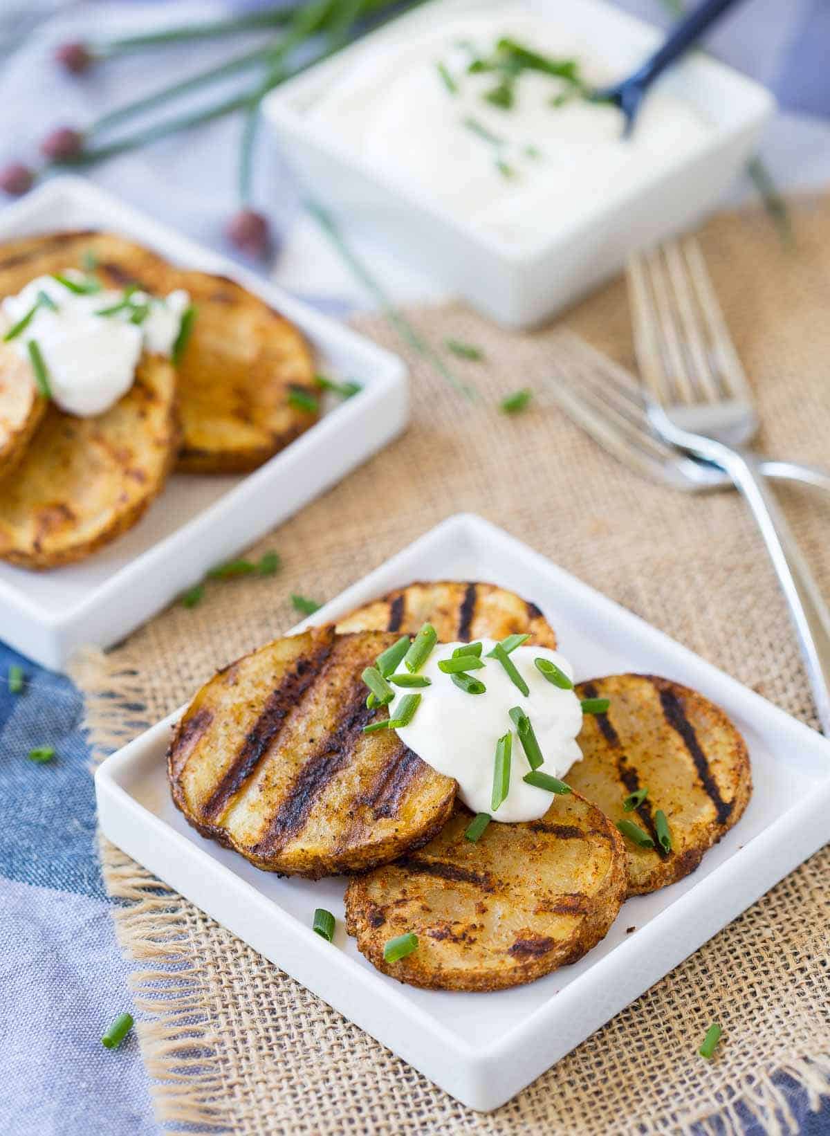 Four potato slices on square white plate, topped with sour cream and chopped chives.