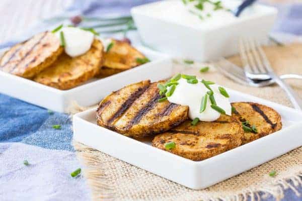 Front view of grilled potatoes on plates with sour cream and chive garnish.