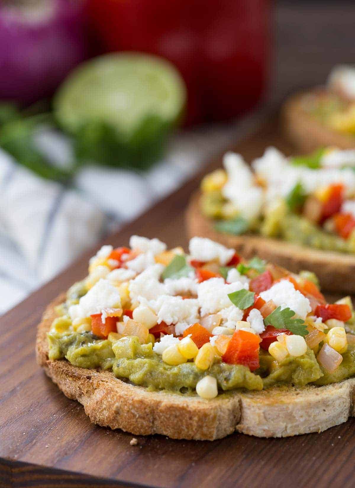 Closeup of guacamole toast on wooden cutting board.