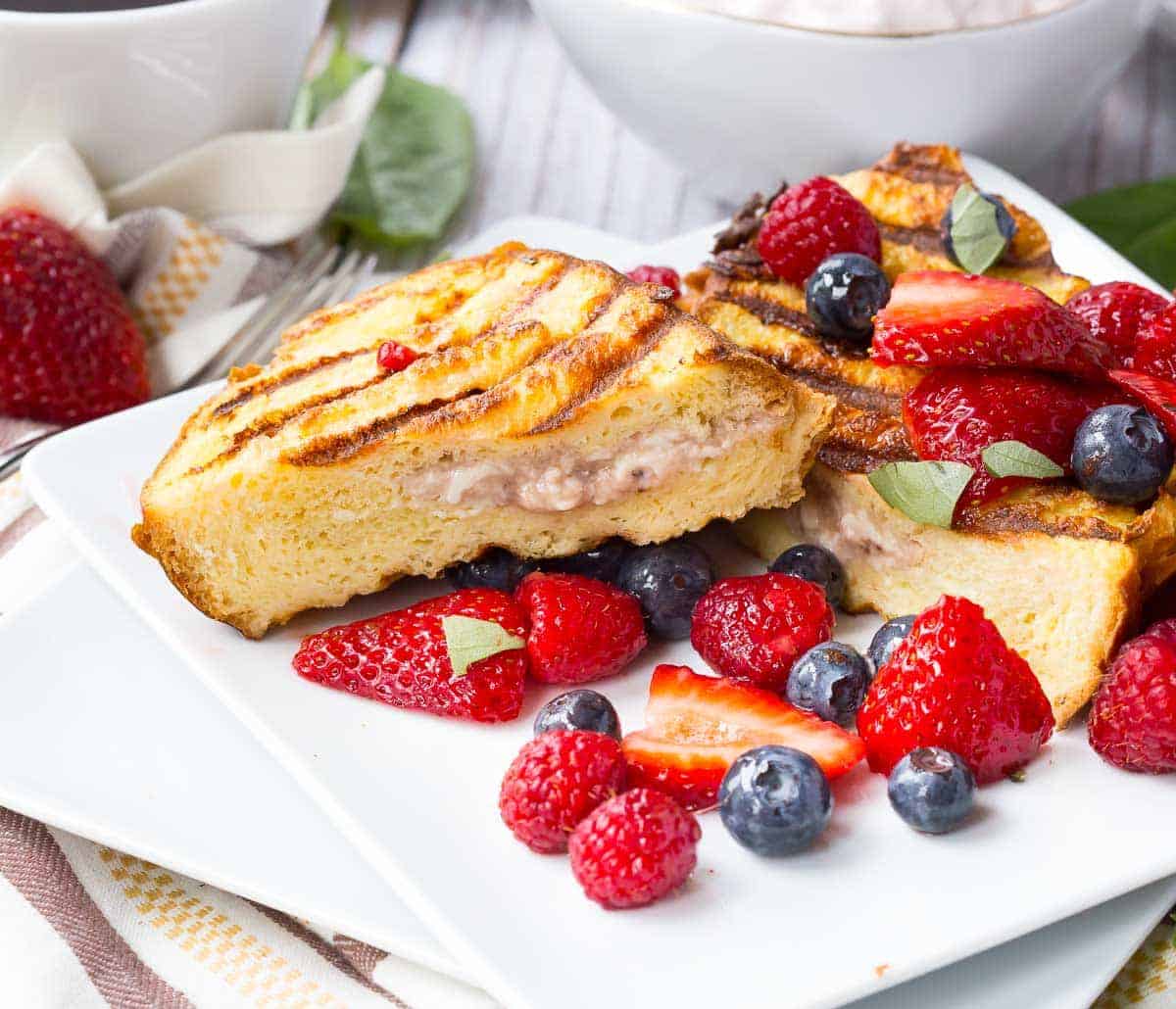Slices of grilled French toast on a square plate garnished with mixed berries.